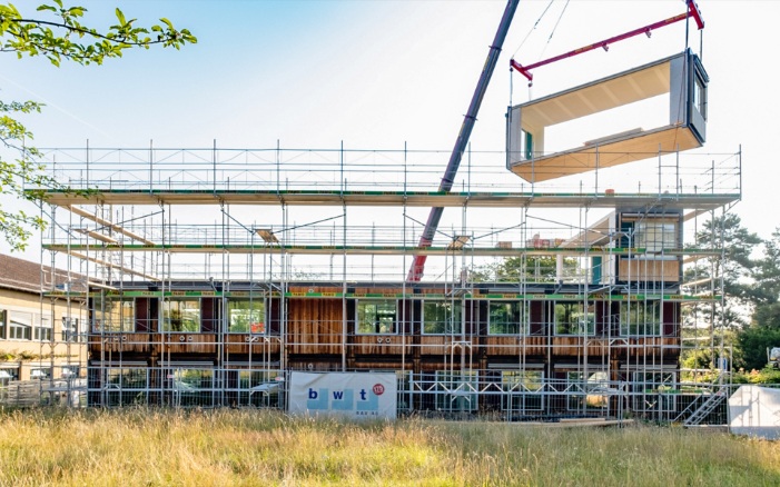 Das bestehende ZM10-Modulbau-Schulhaus Friesenberg wird um ein weiteres Stockwerk erweitert. Ein Holzmodul wird mit dem Kran auf dem Dach platziert. 
