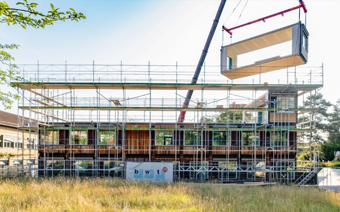 The existing ZM10 modular Friesenberg primary school is extended by adding another floor. A timber module is placed on the roof by crane. 