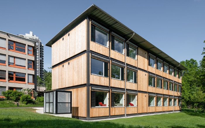 Gesamtansicht des ZM10-Schulpavillons Sihlweid in Zürich auf dem Schulareal und mit Schulhaus im Hintergrund
