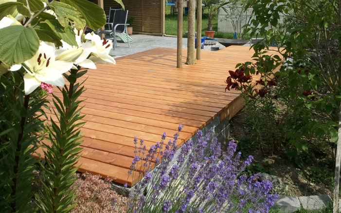 Schöne Holzterrasse mit Blumen und schönem Lavendelstrauch im Vordergrund