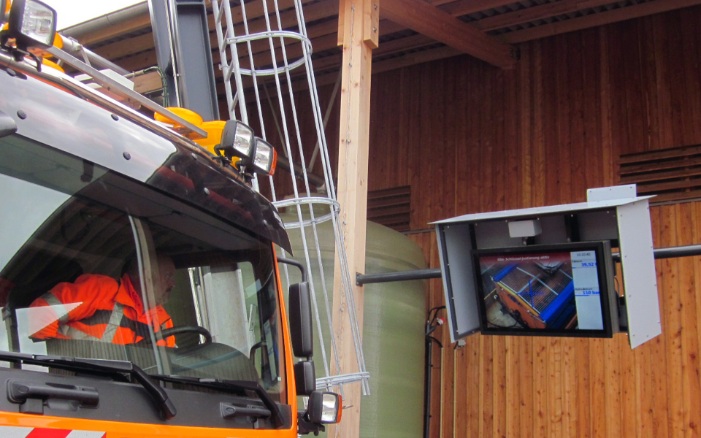 Driver of a winter service vehicle looking out of the cab at the level indicator on screen during the loading process