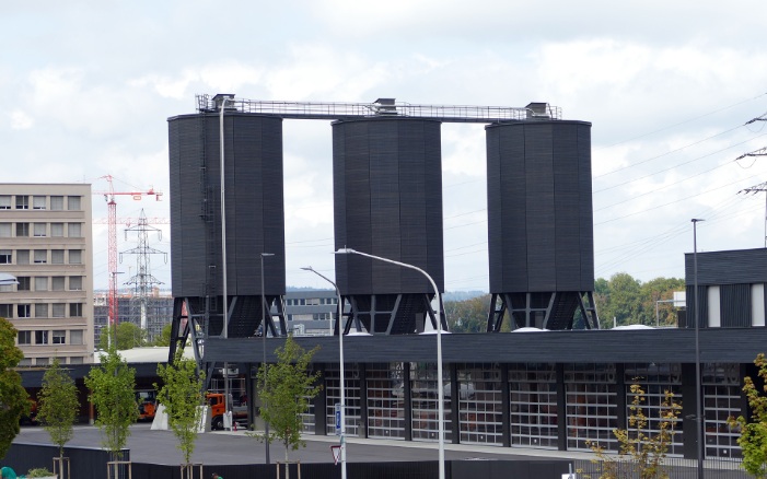 Trois silos dodécagonaux (E12) en bois, reliés avec support en acier et plateforme de toit en bois, placés derrière le parc de camions