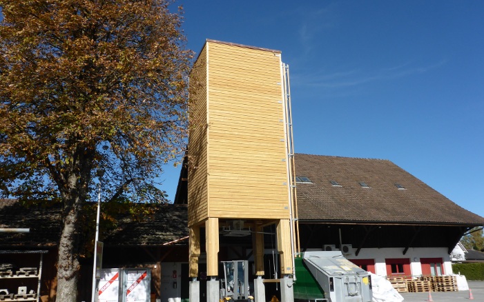Viereckiger 70 m³ Silo (E4) aus Holz mit Holzleiter und Holzunterbau auf Betonsockel vor Bauernhofgebäude platziert