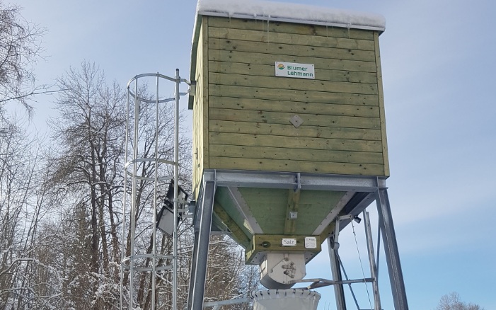 Small, green, four-sided timber silo with steel ladder on steel substructure, in a winter landscape