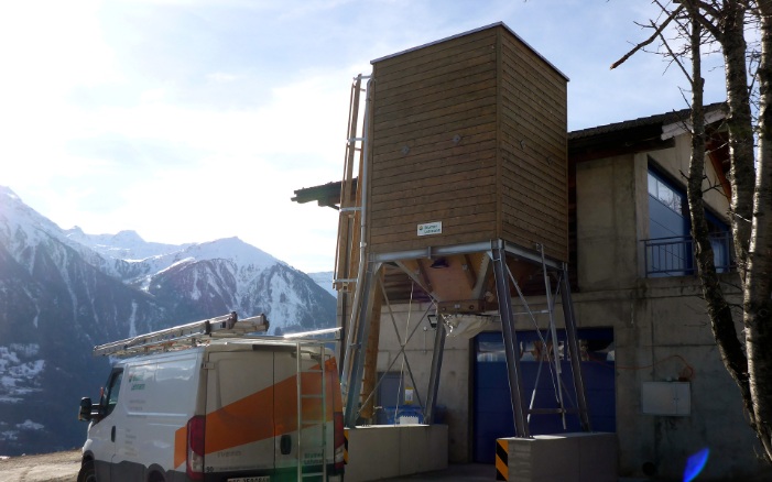 Small 25 m³ four-sided timber silo next to a building and Blumer Lehmann van, in a winter landscape