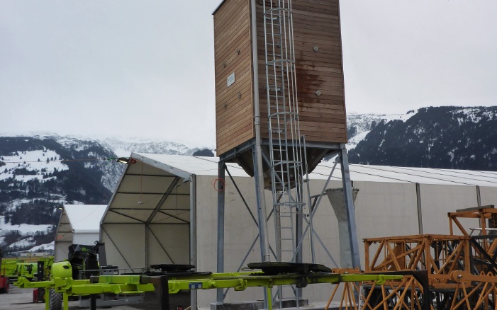 Viereckiger 30 m³ Kleinsilo aus Holz mit Stahlleiter und Stahlunterbau neben weisser Zelthalle platziert