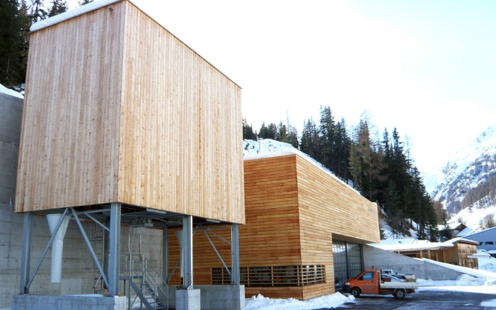 100 m³ timber modular silo with steel substructure, alongside a maintenance depot building with identical facade