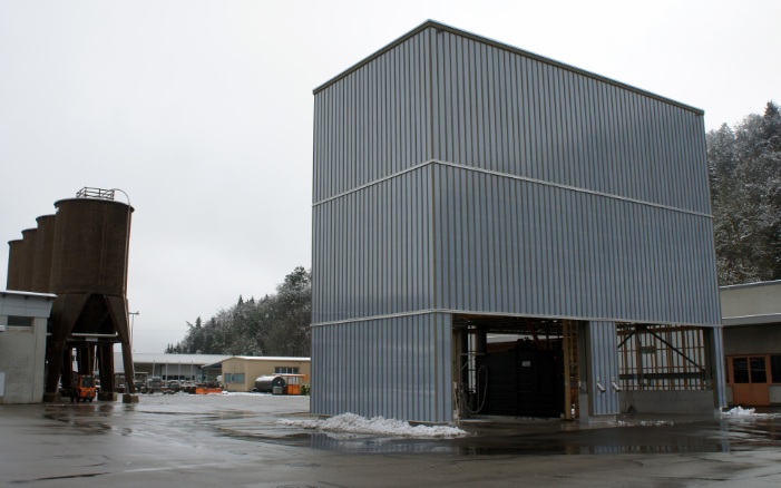 Architektonischer hellgrauer 400 m³ Modulsilo neben vier zwölfeckigen Silos aus Holz auf Werkhofareal platziert