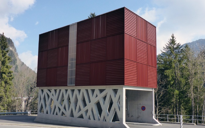 Silo modulaire architectural rouge avec support en béton filigrane, traversé par une route