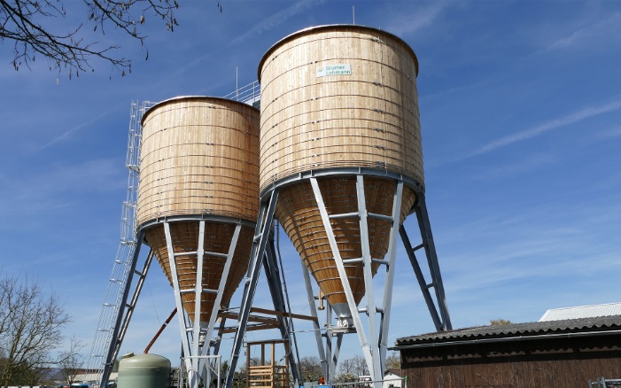 Zwei runde 350 m³ Silos aus Holz mit Stahlleiter und grauem Stahlunterbau auf Werkhofareal platziert