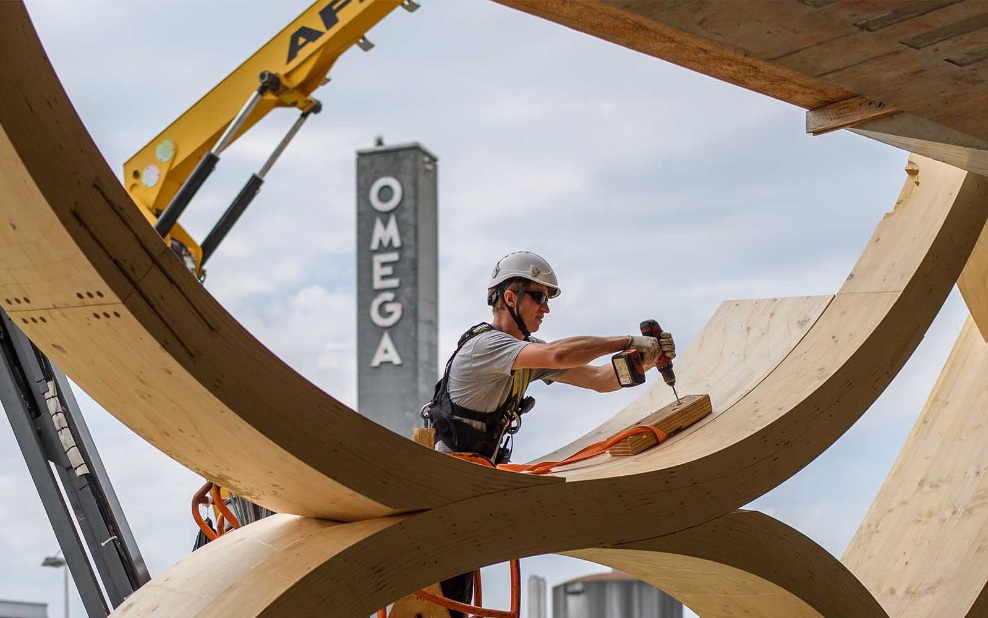 Der Montagemitarbeitende bohrt ein Loch in die Holzkonstruktion des Swatch-Gebäudes