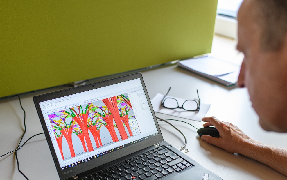 A man sits at a laptop working on a 3D parametric model