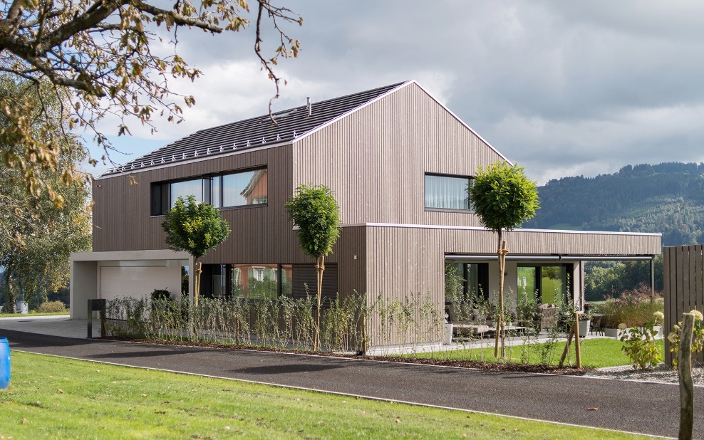 Gesamtaufnahme Einfamilienhaus mit Seeblick sowie begrünte Umgebung und Zufahrtsstrasse zum Eingang und Garage