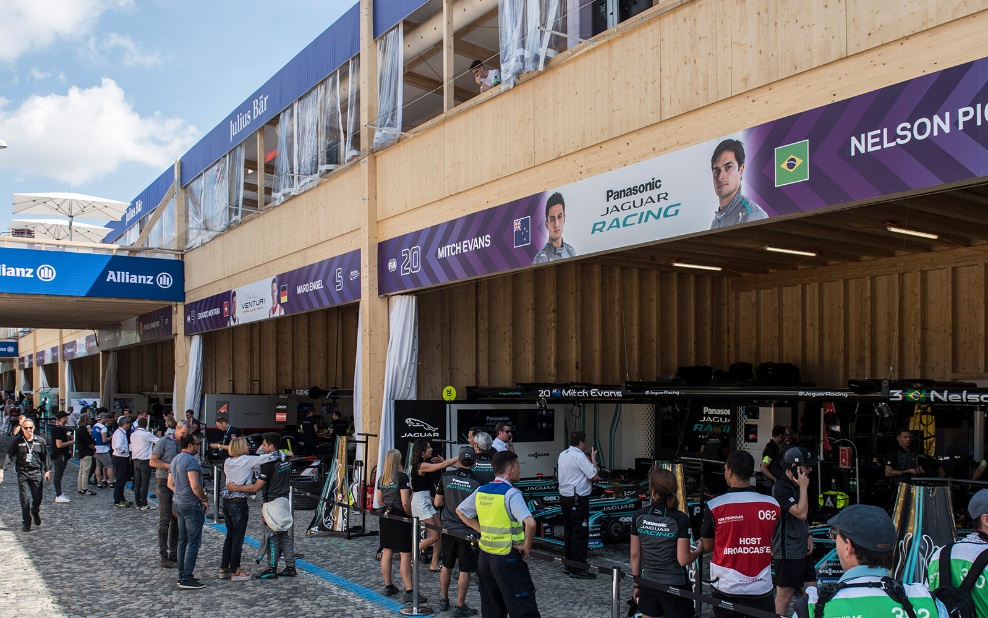 Der Eventbau aus Holz diente am Zürich E-Prix 2018 als Boxengasse. Im Vordergrund sind Besucher und Teammitglieder zu sehen. Im Hintergrund stehen die Rennautos in den Boxen. 