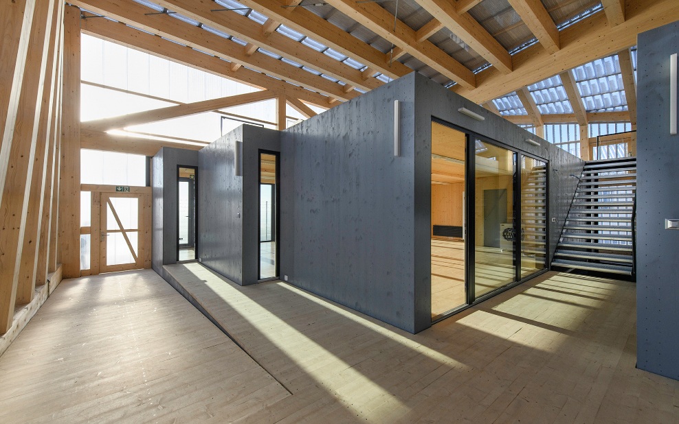 Raumgrosse Holzmodule definieren Raumeinheiten in einer Holzhalle.