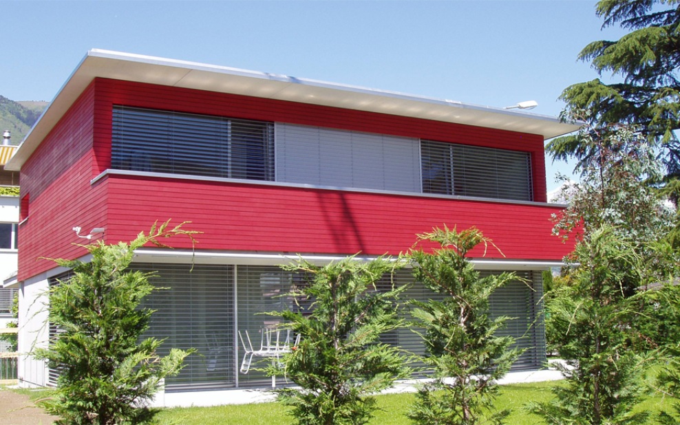 Vollansicht eines Einfamilienhauses, bei dem eine rote Rhomboidschalung mit Nut und Kamm verbaut wurde.