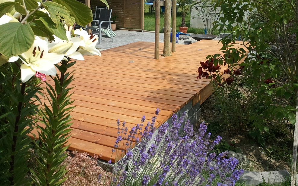 Schöne Holzterrasse mit Blumen und schönem Lavendelstrauch im Vordergrund