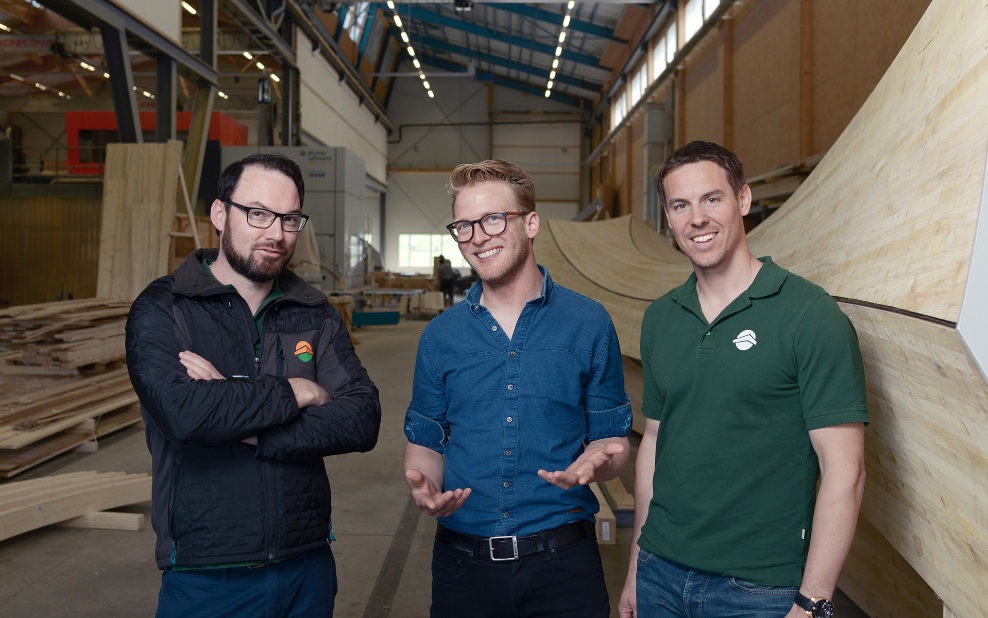 Gruppe von Quereinsteigern in der Produktionshalle mit einem Holzobjekt im Hintergrund