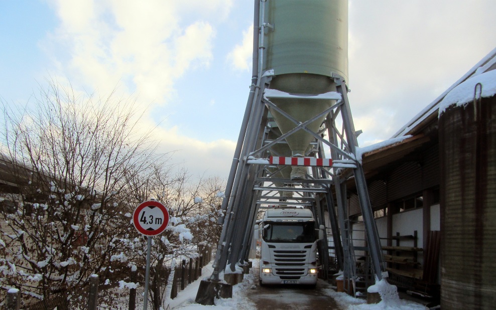 Drei grüne GFK-Silos hintereinander platziert, darunter steht ein Lastwagen, welcher beladen wird