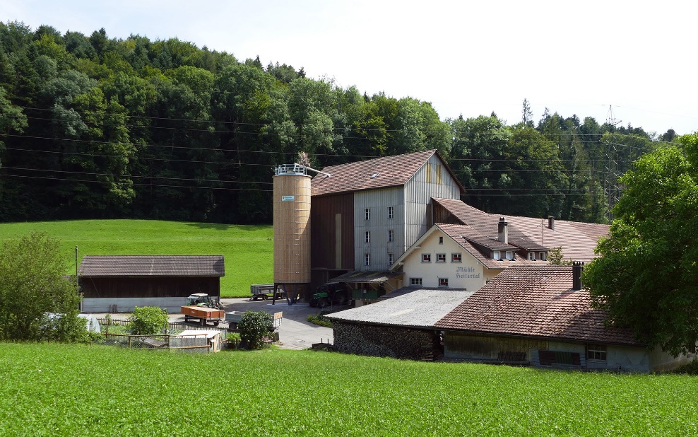 Round timber storage silo for grain, alongside a mill