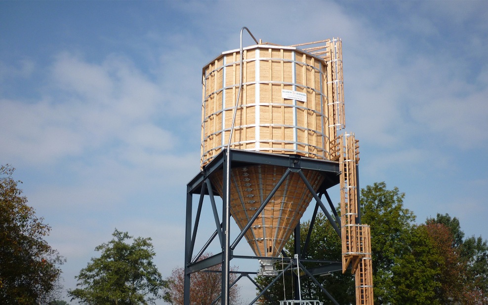 Twelve-sided timber silo (E12) with wooden ladder and grey steel substructure, in front of a group of trees