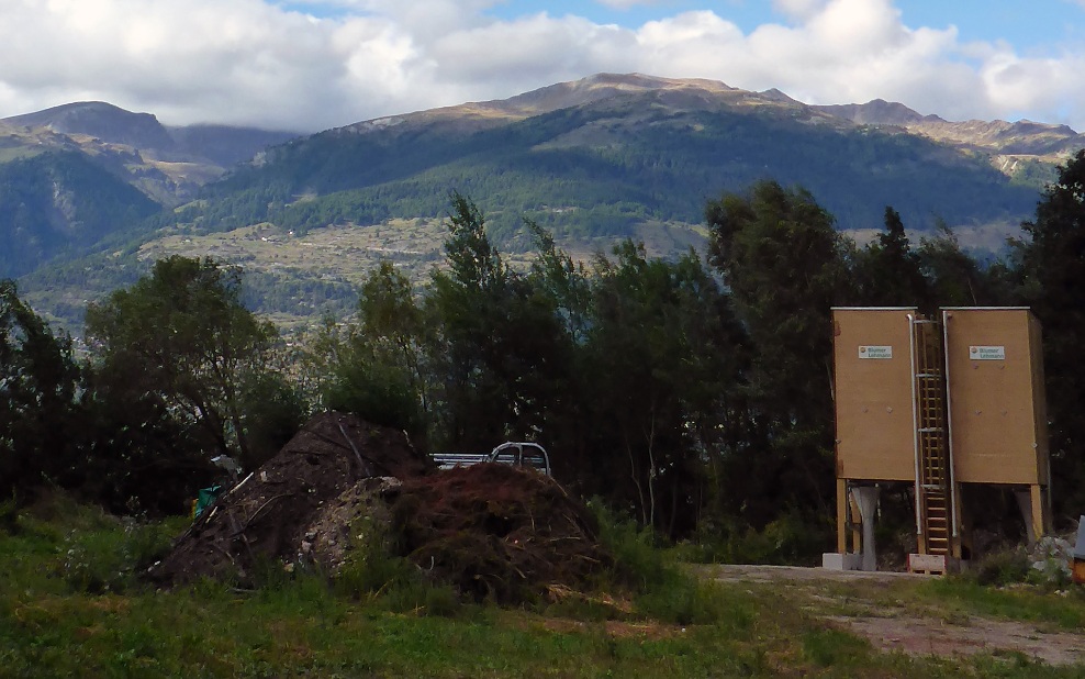 Two 20 m³ four-sided timber silos with wooden ladder and wooden substructure, in a clearing