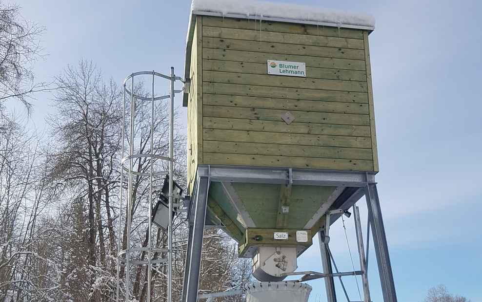 Petit silo carré vert en bois avec échelle en acier sur un support en acier dans un paysage hivernal