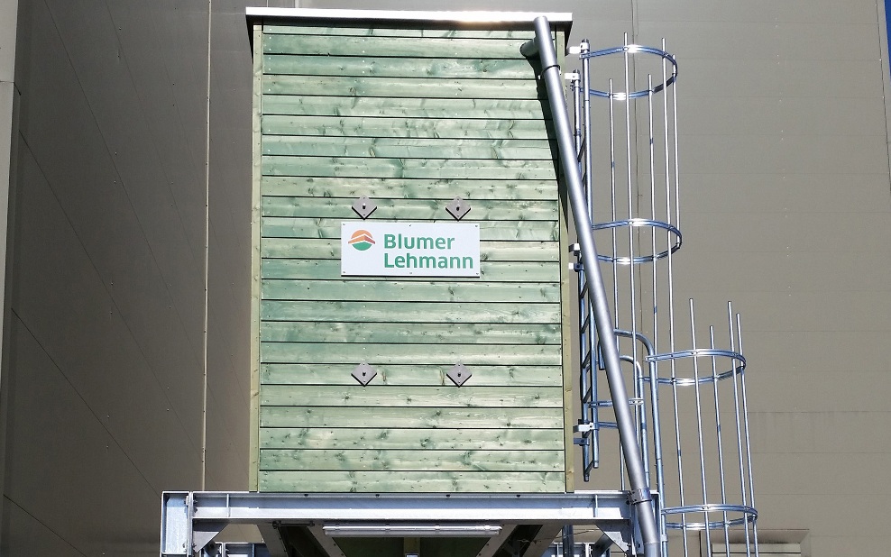 Small, green, four-sided timber silo with steel ladder and steel substructure