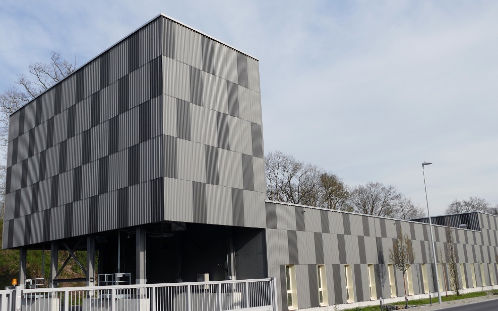 Architektonischer 250 m³ Modulsilo mit hell- und dunkelgrau karierter Fassade aus Holz optisch integriert in einen grösseren Gebäudekomplex.