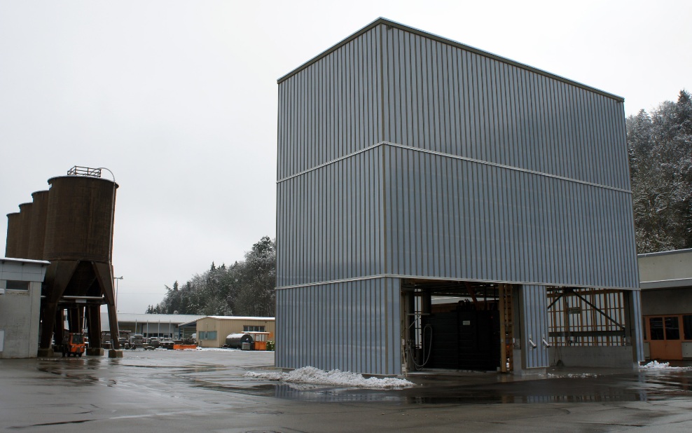 Architektonischer hellgrauer 400 m³ Modulsilo neben vier zwölfeckigen Silos aus Holz auf Werkhofareal platziert