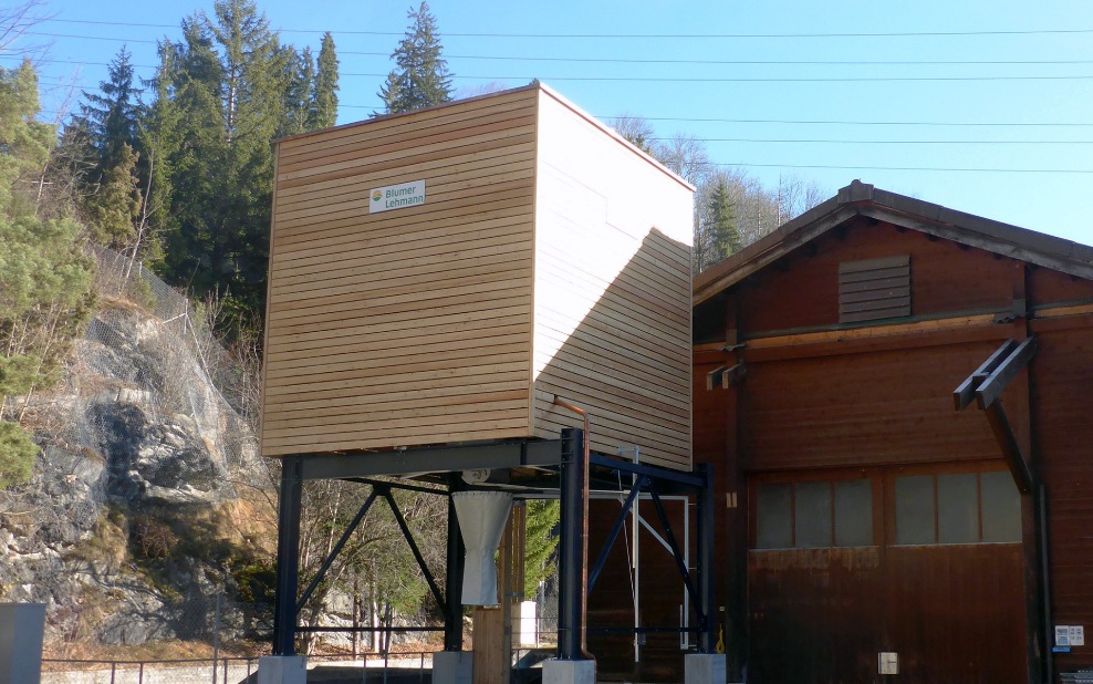 Silo modulaire en bois de 50 m³ avec support en acier gris, accolé à un bâtiment en bois existant