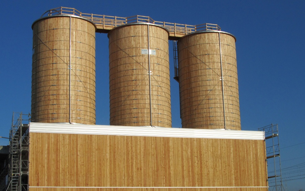 Trois silos ronds en bois de 300 m³ intégrés dans un bâtiment en bois et reliés par une passerelle de toit