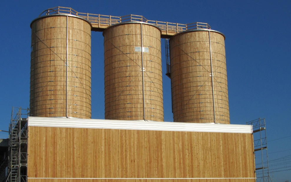 Three 300 m³ round timber silos integrated into a timber building, connected by a wooden roof crossover