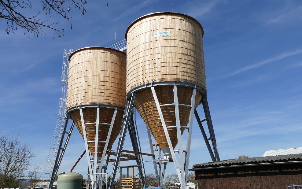 Two 350 m³ round timber silos with steel ladder and grey steel substructure, at a maintenance depot