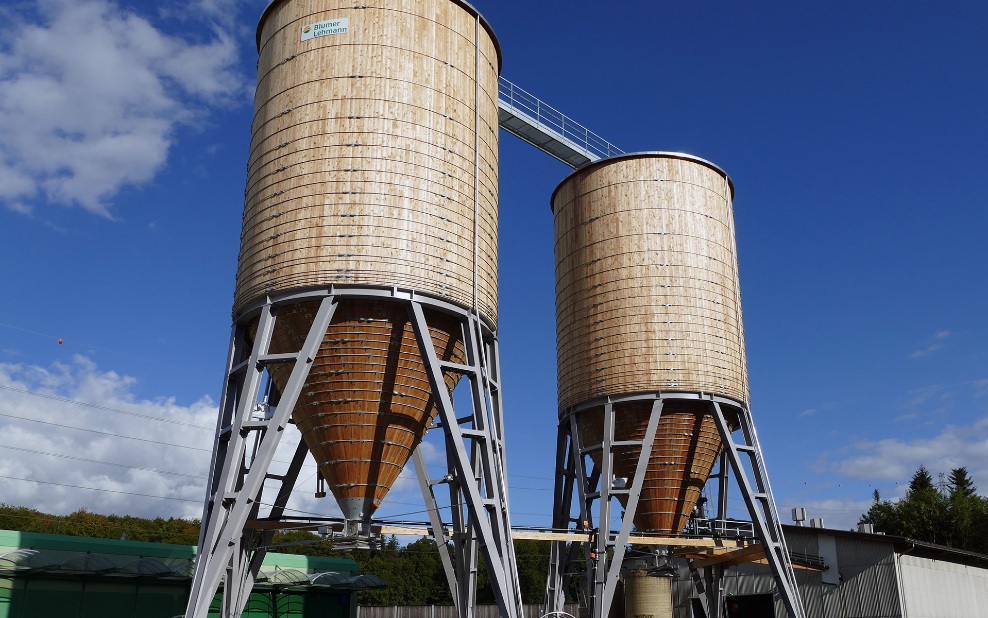 Zwei runde 500 m³ Silos aus Holz mit schwarzem Stahlunterbau auf Betonsockel im Werkhofareal platziert