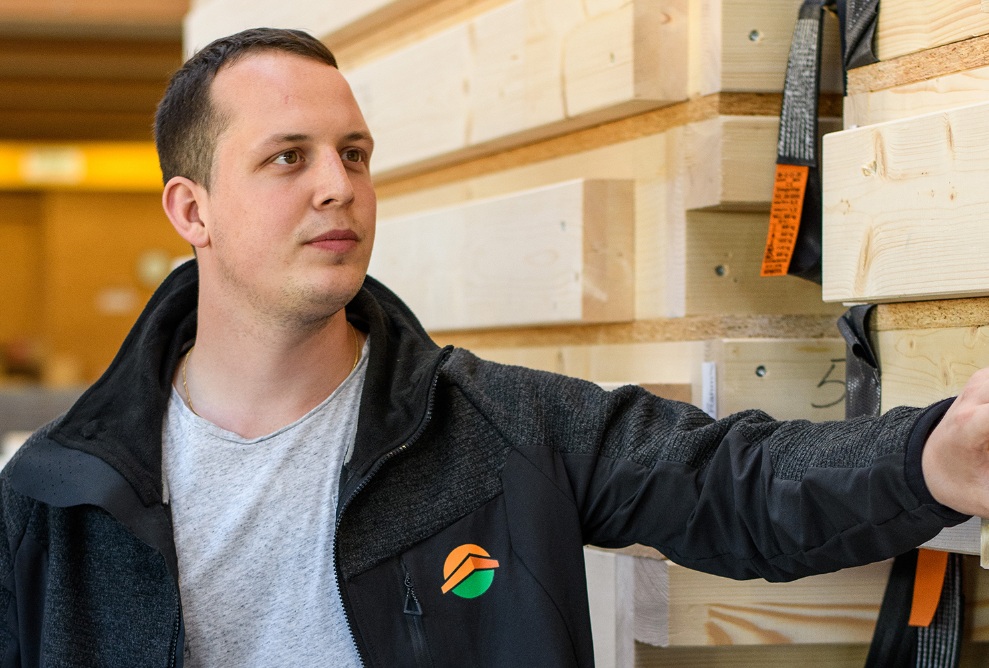 Ein junger Mann mit steht vor gefertigten Wandelementen und prüft diese mit konzentriertem Blick auf der Ladebritsche. 