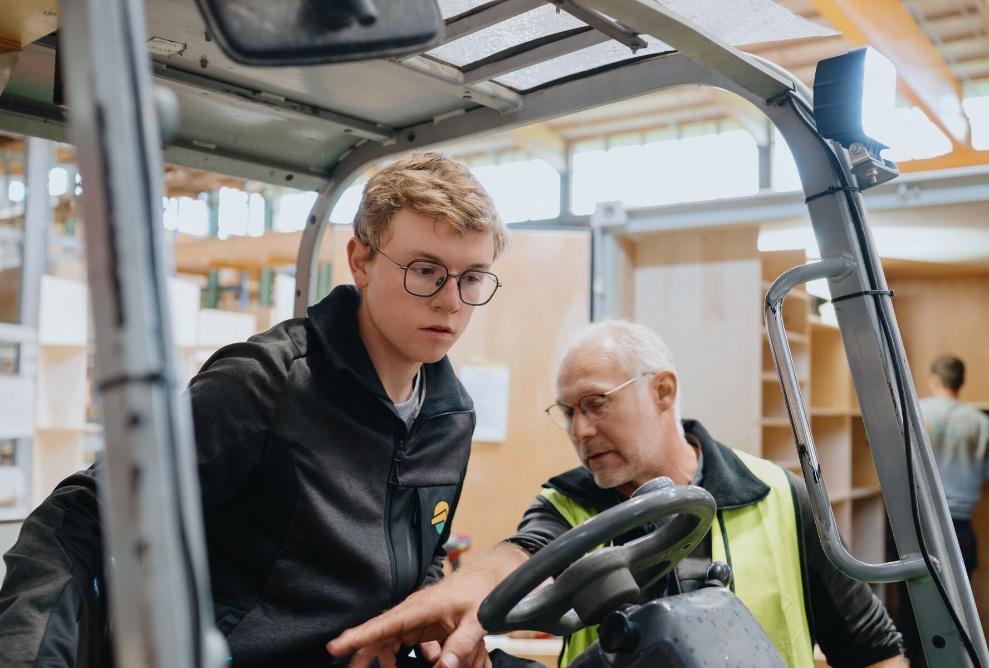 Portrait photo of forklift driver Dominik Dörig, with forklift and Erlenhof in the background