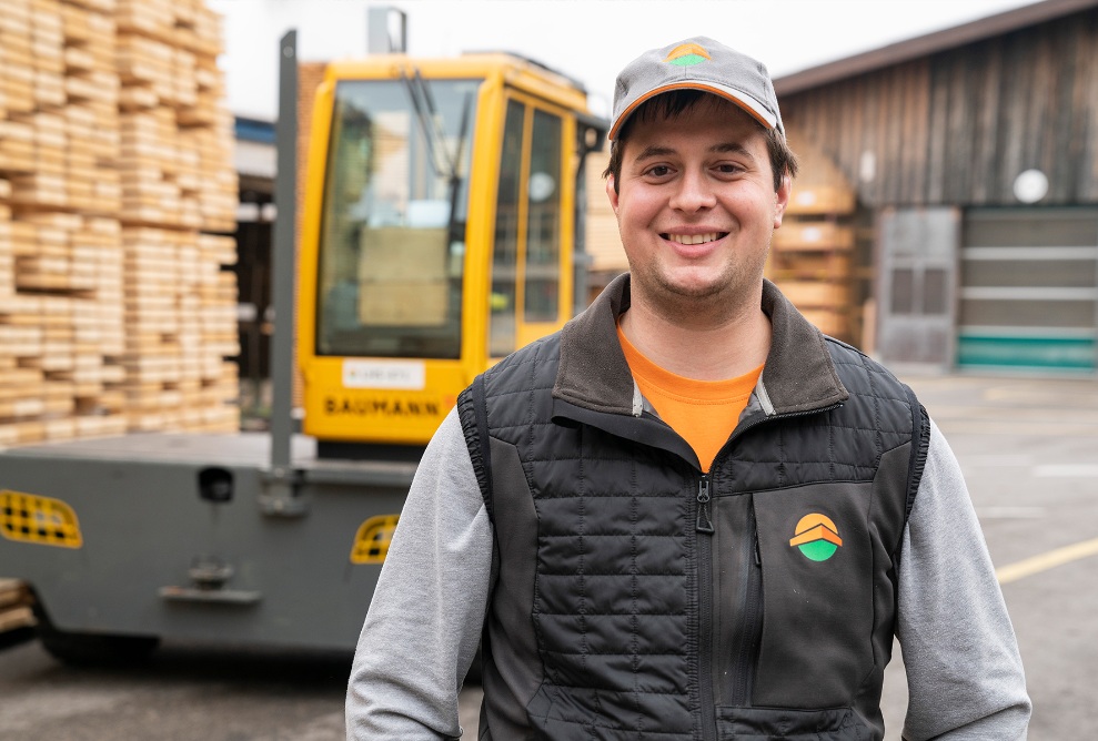 Portrait photo of forklift driver Dominik Dörig, with forklift and Erlenhof in the background