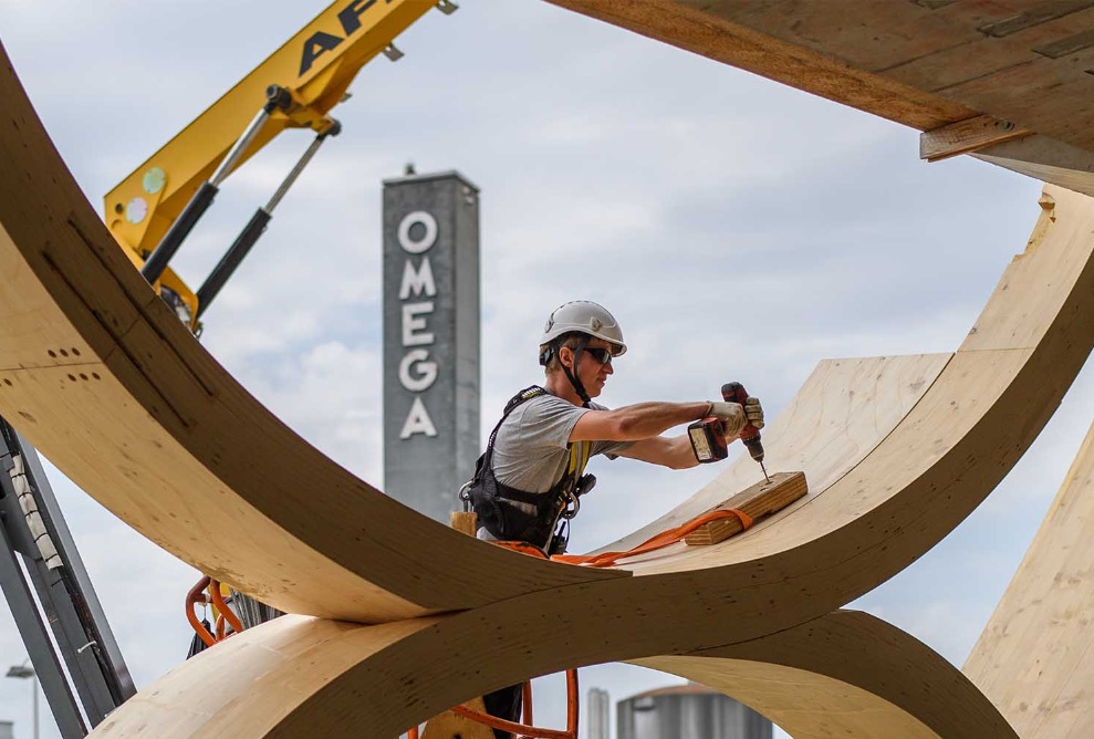 Der Montagemitarbeitende bohrt ein Loch in die Holzkonstruktion des Swatch-Gebäudes