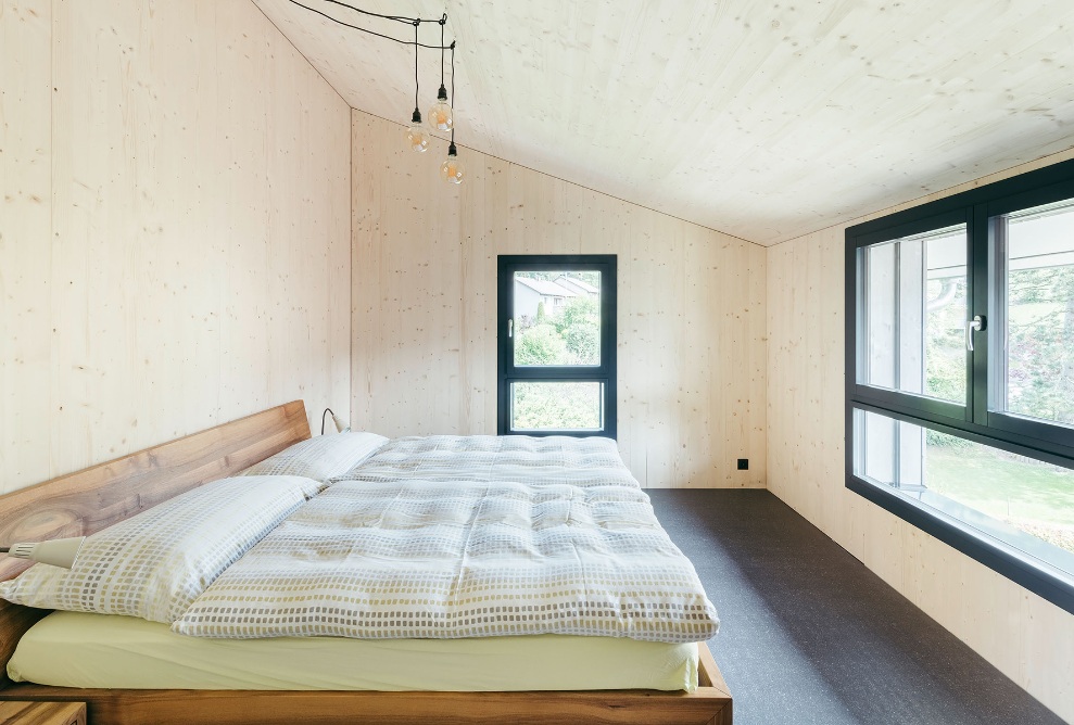 Innenansicht Schlafzimmer mit Holzbett, einer langen Fensterfront und einem schmalen Einzelfenster