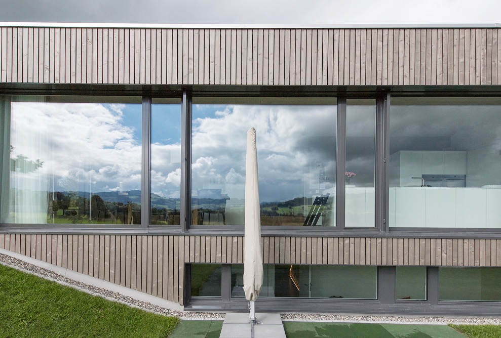 Vue latérale de la façade vitrée de la maison individuelle avec vue sur la salle à manger ouverte et la cuisine