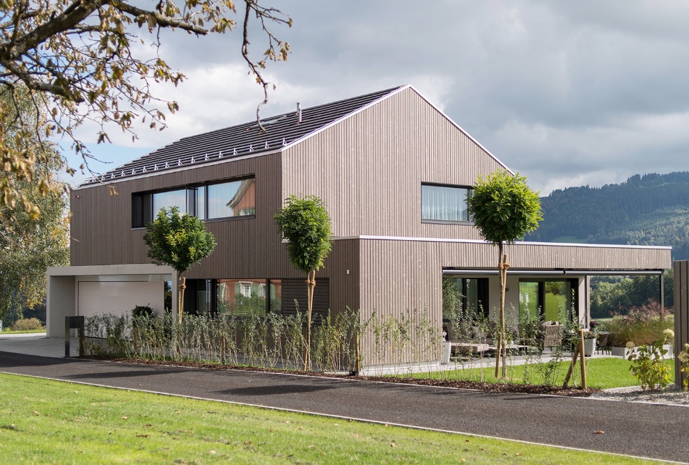 Gesamtaufnahme Einfamilienhaus mit Seeblick sowie begrünte Umgebung und Zufahrtsstrasse zum Eingang und Garage