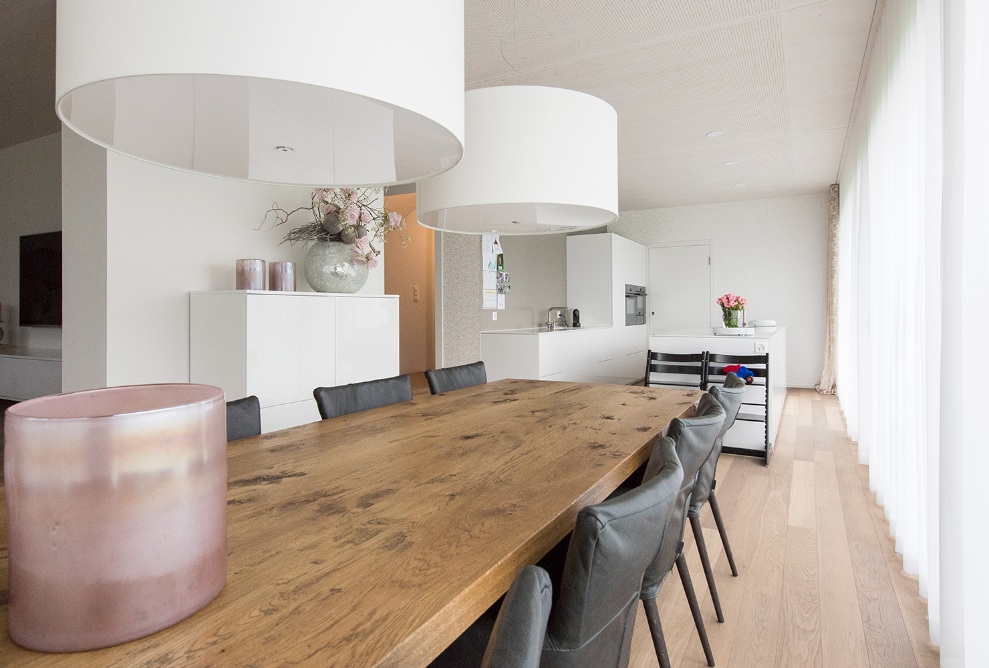 The photograph shows the interior of the single-family house with lake views. Fitted out with a dining room and long dining table in dark wood as well as a bright kitchen and open living room.