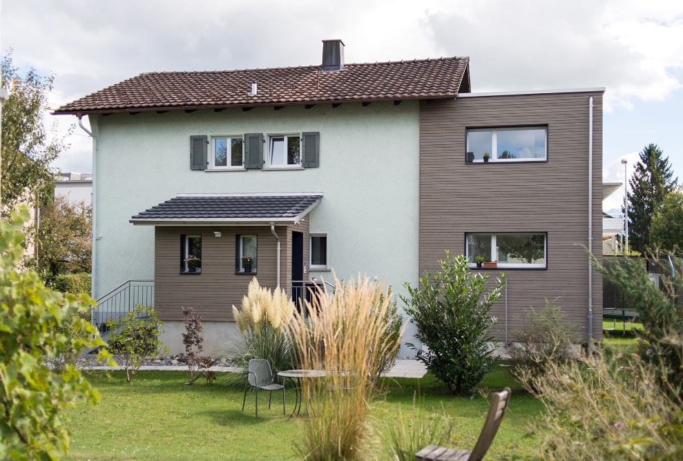 Side view of the single-family home with entrance, new extension and garden.