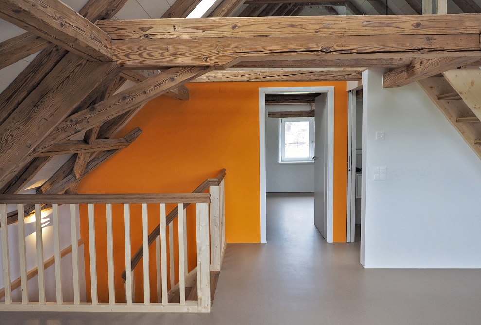 Aufnahme zeigt das grossräumige Dachgeschoss mit Zugang zu weiteren Zimmern, zwei komplett aus Holz ausgestatteten Treppen und den breiten Holzbalken.