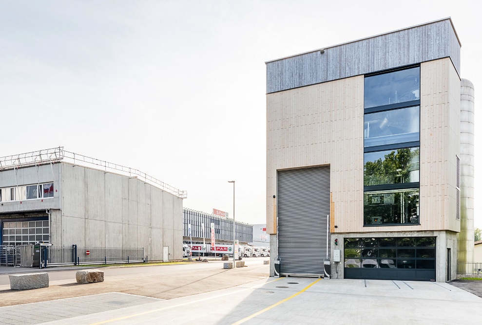 Overall view of the energy plant from the front with visibly different facade treatments. The lower section is treated with UVood, the upper is pre-greyed.