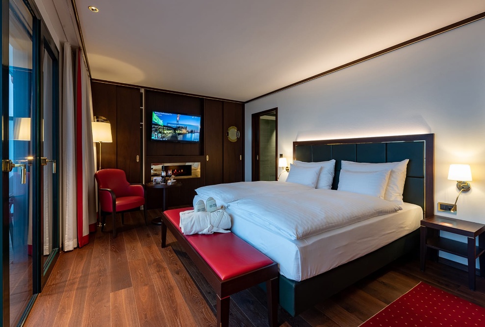 Interior view of a guest room at Hotel Bad Horn with a double bed, a red bench and a dark-coloured wardrobe in the background.