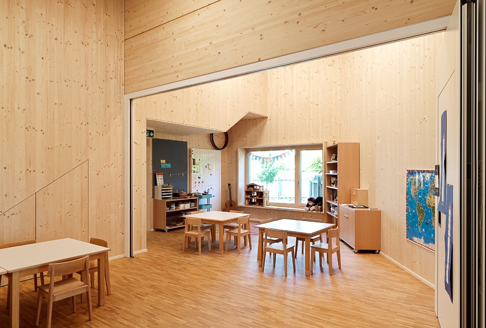 Interior view of the classroom in the converted Wittenbach Kindergarten. The room’s walls, floor and ceiling are made of timber. The room can be split into two with a folding wall. 