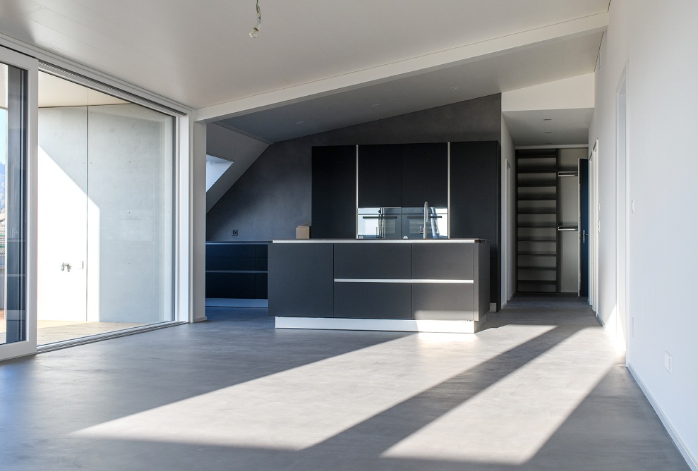 View of an open kitchen with sloped ceiling and the living area as well as the wooden terrace flooring and staircase