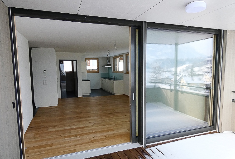 Vue du salon et de la salle à manger avec cuisine à travers les portes ouvertes du balcon